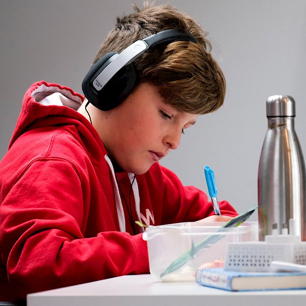 Student wearing headphones writing in front of laptop