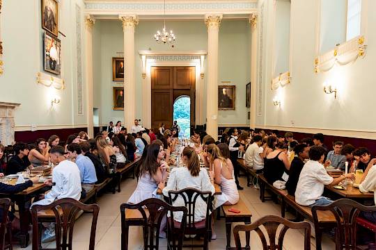 Students seated together in an Oxford college dining hall, sharing a meal beneath high ceilings and traditional wooden panelling, capturing the authentic university atmosphere.