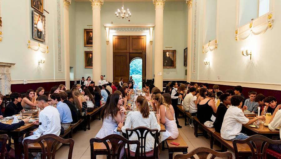Students seated together in an Oxford college dining hall, sharing a meal beneath high ceilings and traditional wooden panelling, capturing the authentic university atmosphere.